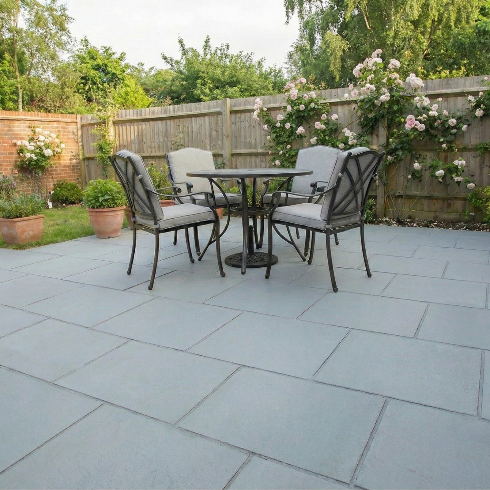 Outdoor patio with a round table and chairs on a stone patio, surrounded by greenery.